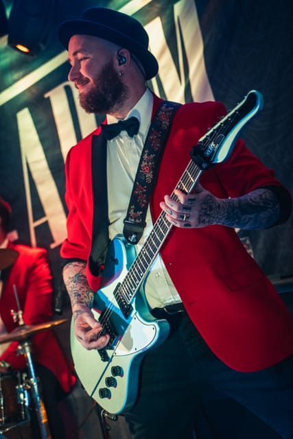 The guitarist in a red jacket and top hat, mid-song
