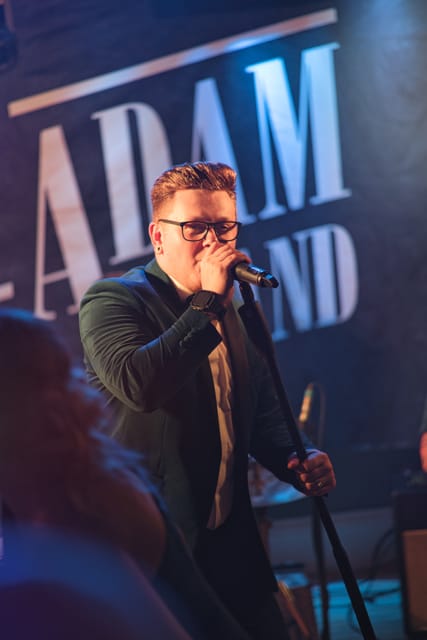 Adam at the microphone in front of the band backdrop